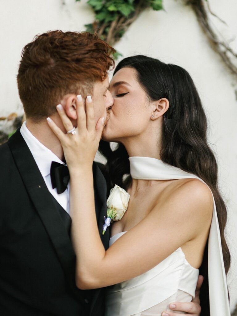 Close-up of a romantic bride with Hollywood waves sharing a passionate kiss with her groom, highlighting a timeless moment for editorial wedding photography.