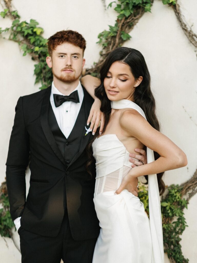 Elegant bride in a strapless corset wedding dress with a chic neck scarf posing naturally with her groom, capturing high-end style for editorial wedding photography.