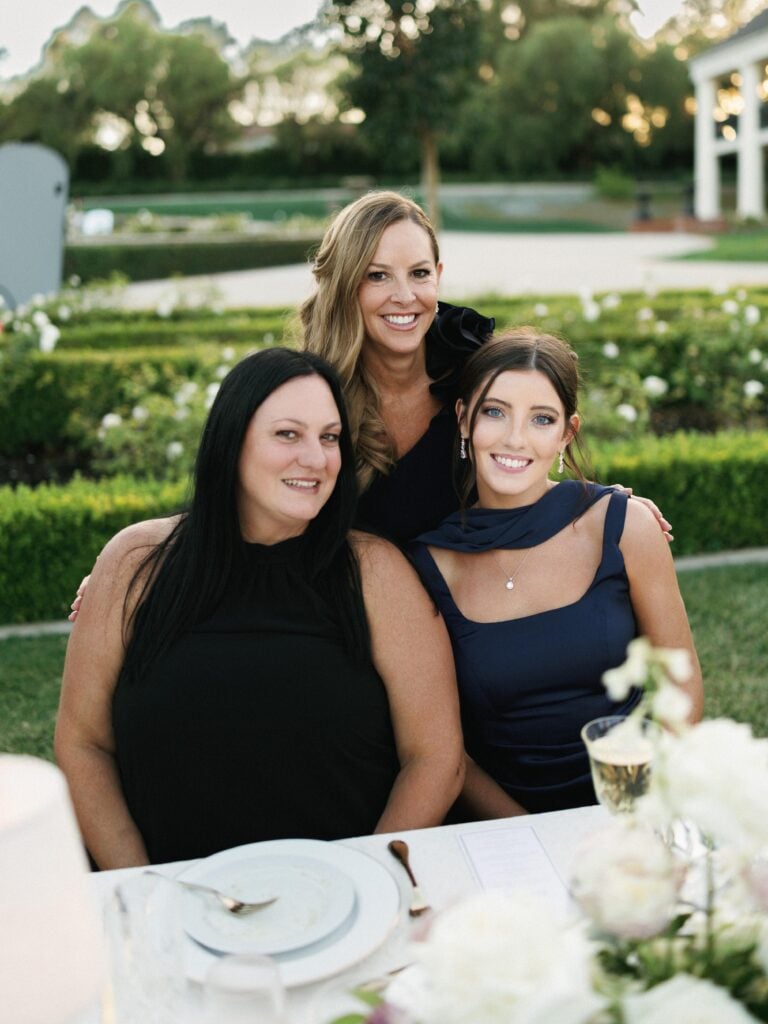Chic wedding guests in elegant black and navy attire posing at a beautifully styled reception table during high-end wedding weekend coverage.