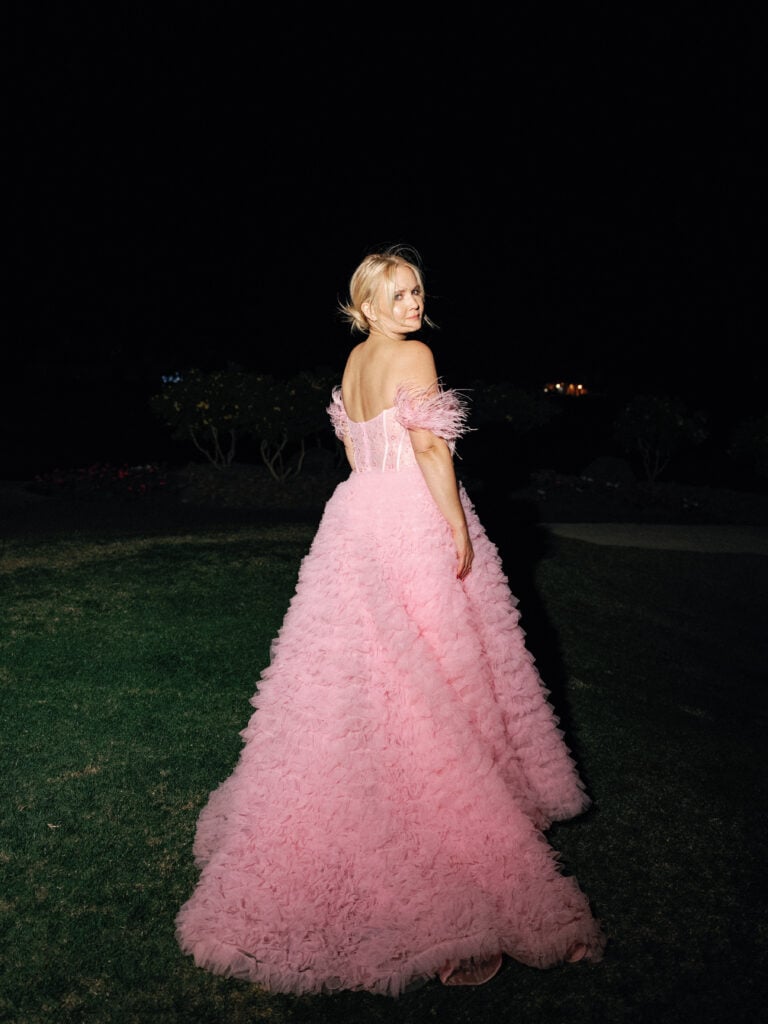 Stunning bride showcasing a pink tulle ruffle wedding dress with feather off-the-shoulder straps during an outdoor night event featured in wedding weekend coverage.