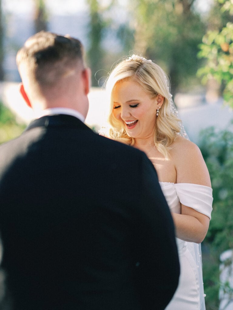 Bride in an off-the-shoulder wedding dress reading vows to her groom, captured on film by a Palm Springs wedding photographer.