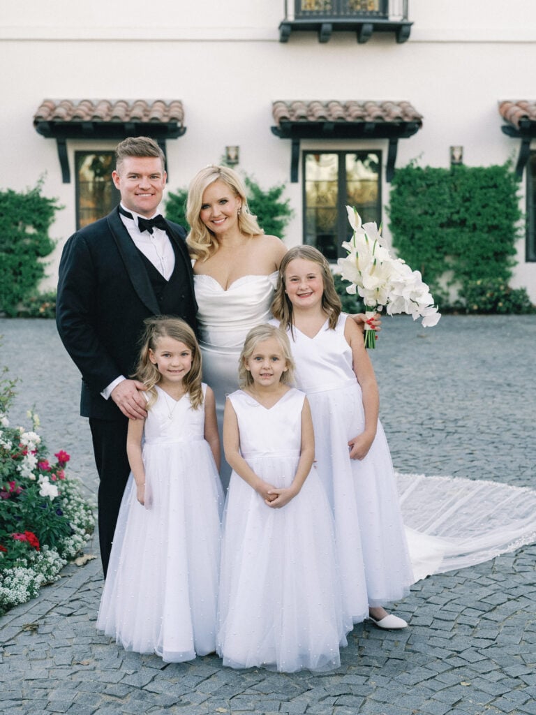 Bride and groom posing with three flower girls in white dresses, shot on film by a Palm Springs wedding photographer.