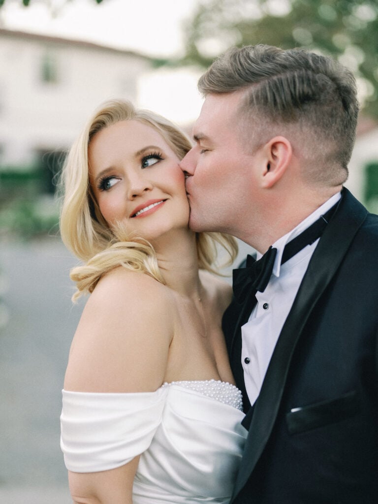 Close-up of a groom kissing his bride's cheek, showcasing her off-the-shoulder wedding dress, shot on film by a Palm Springs wedding photographer.