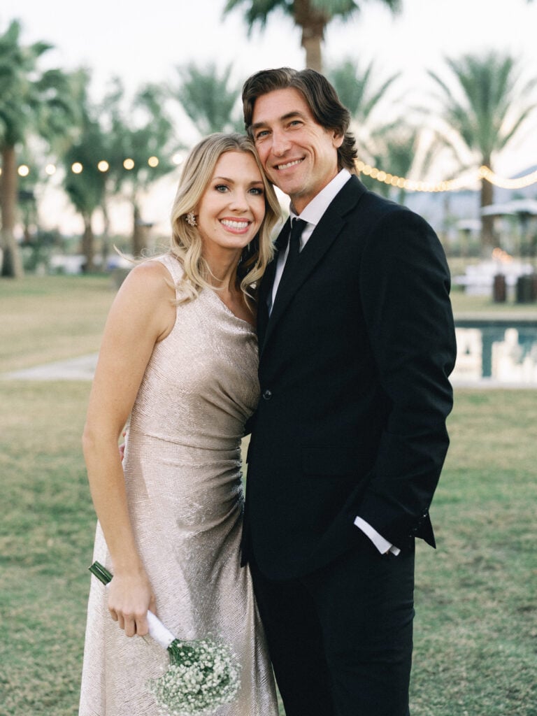 Wedding guests in a black suit and a gold sparkly dress posing on a lawn, shot on film by a Palm Springs wedding photographer.