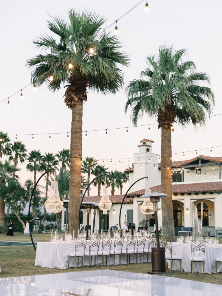 Outdoor wedding reception tables and white dance floor under palm trees with string lights, captured on film by a Palm Springs wedding photographer.