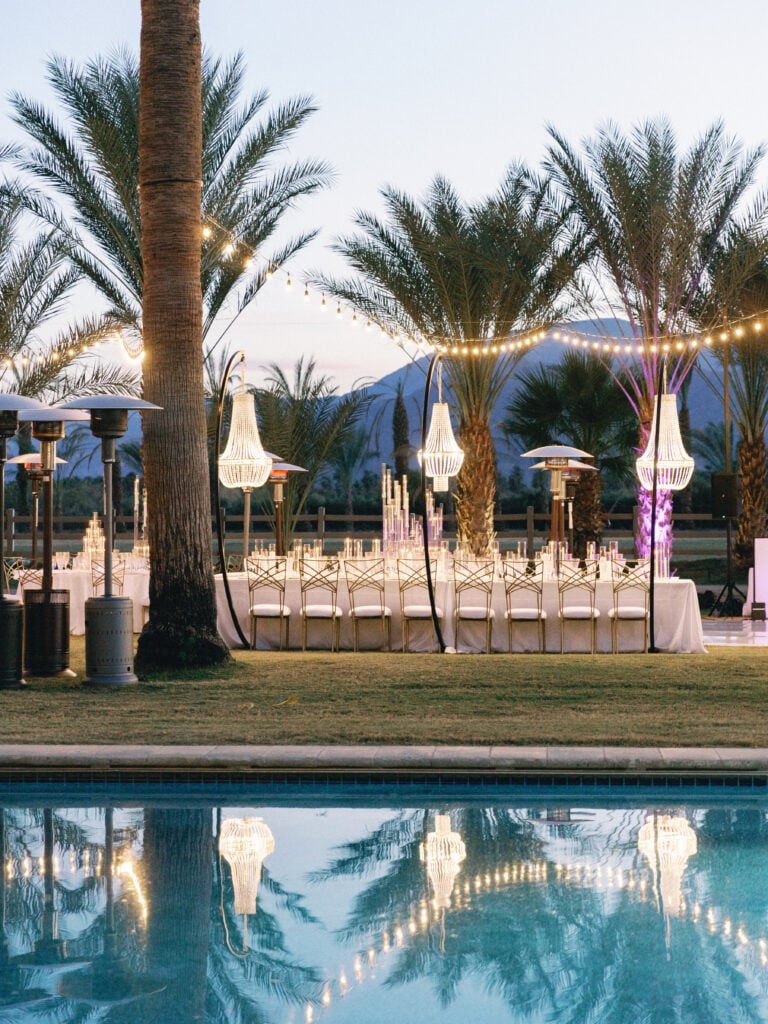 Outdoor wedding reception setup next to a swimming pool with hanging chandeliers and string lights, captured on film by a Palm Springs wedding photographer.
