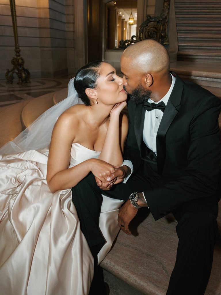 Intimate late-night wedding photo ideas capturing a romantic kiss between a black-tie groom and his bride on marble steps.