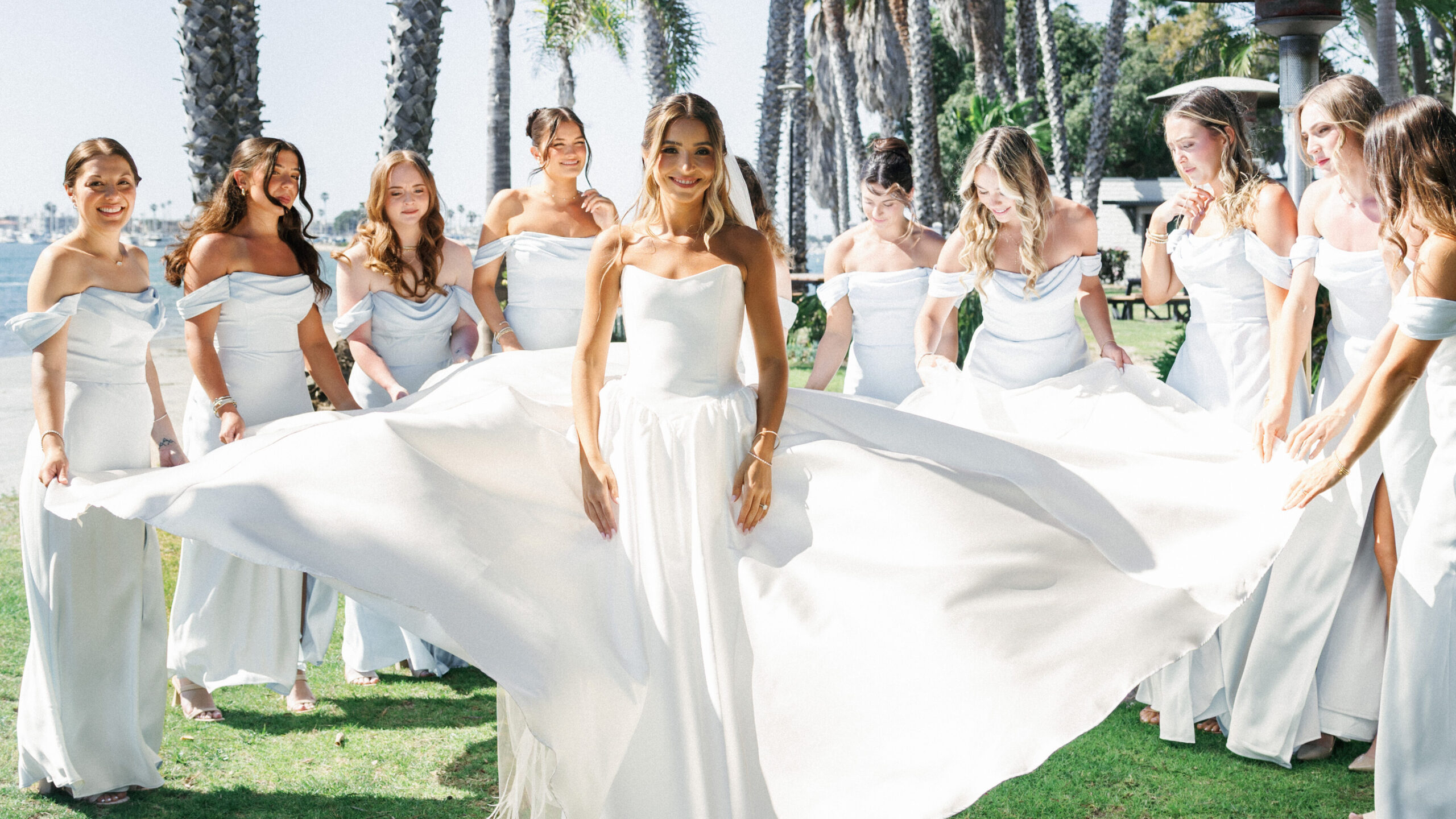 Creative wedding photo ideas featuring bridesmaids in elegant off-the-shoulder blue gowns holding the bride's voluminous train.