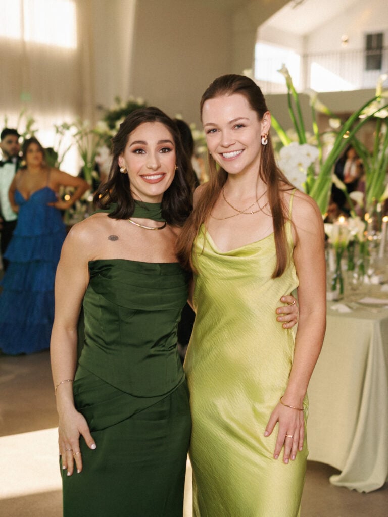 Chic female wedding guests posing in a strapless emerald green dress and a chartreuse silk cowl neck gown during premium wedding weekend coverage.