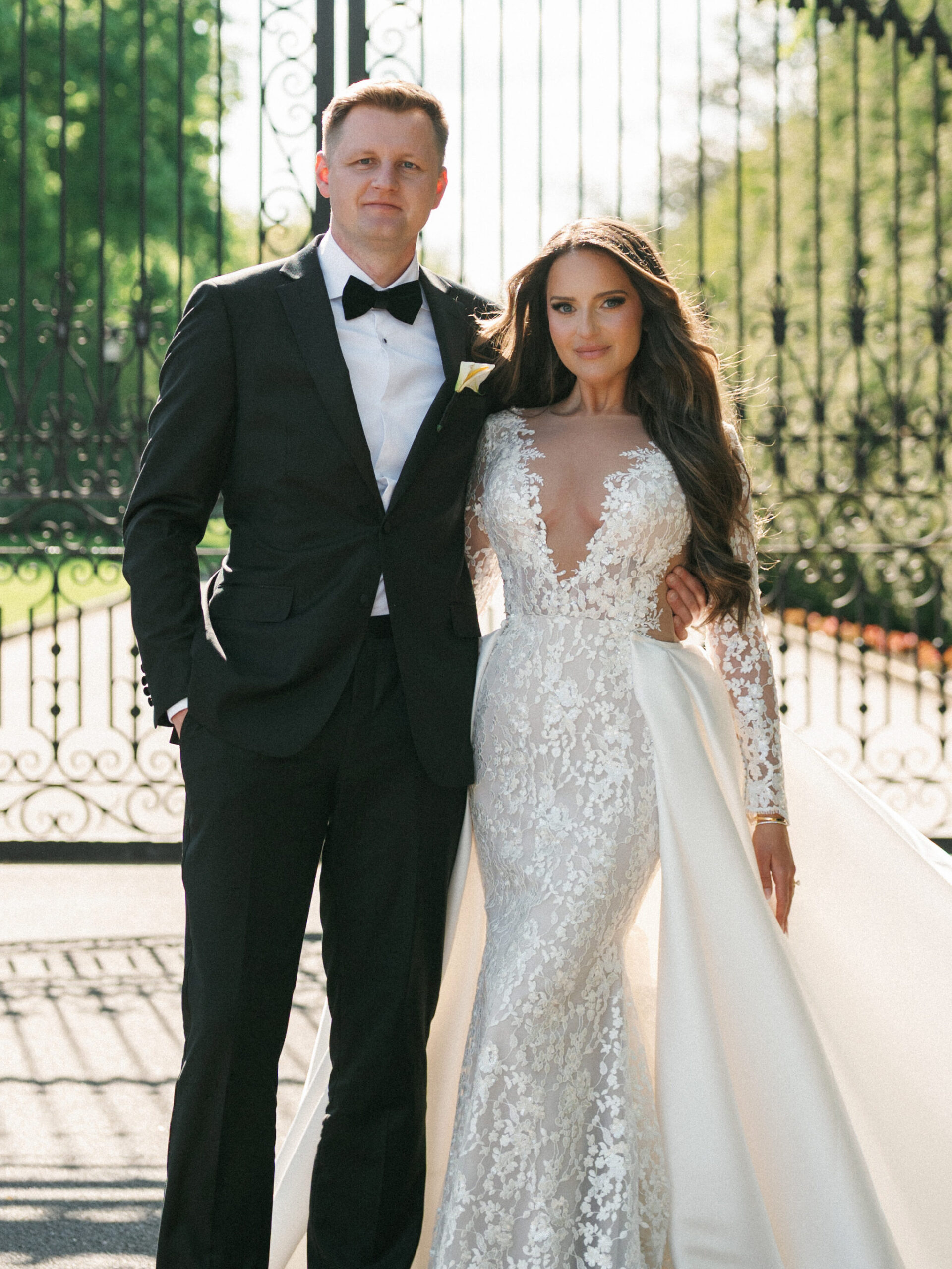 Sophisticated wedding photo ideas capturing a couple posing in front of tall gates, highlighting the bride's lace illusion gown.