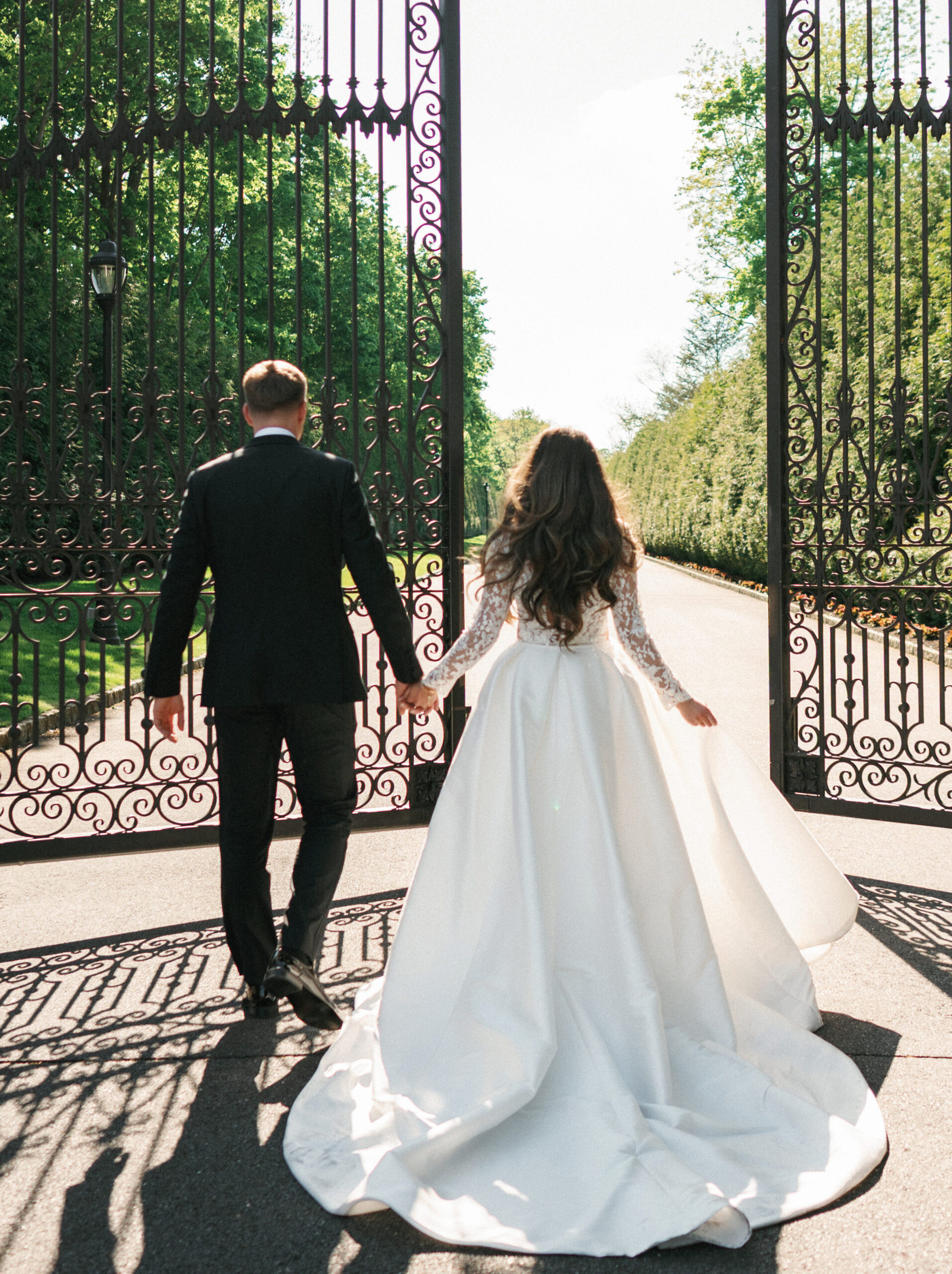 Grand estate wedding photo ideas featuring a bride and groom walking hand-in-hand through historic wrought iron gates.