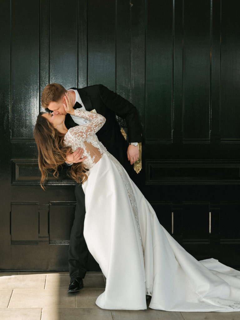 Romantic outdoor wedding photo ideas featuring a stunning wedding dip kiss that highlights the movement of a satin overskirt.