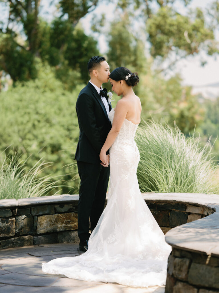 Romantic film wedding portrait of a groom kissing his bride's forehead on a stone terrace, captured by a Napa Valley wedding photographer.