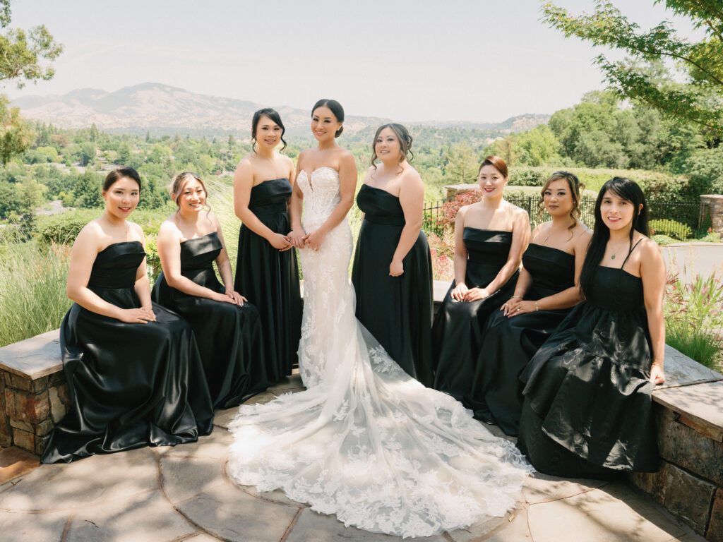 Bridesmaids in elegant black strapless gowns posing with a chic bride on a terrace, captured on film by a Napa Valley wedding photographer.