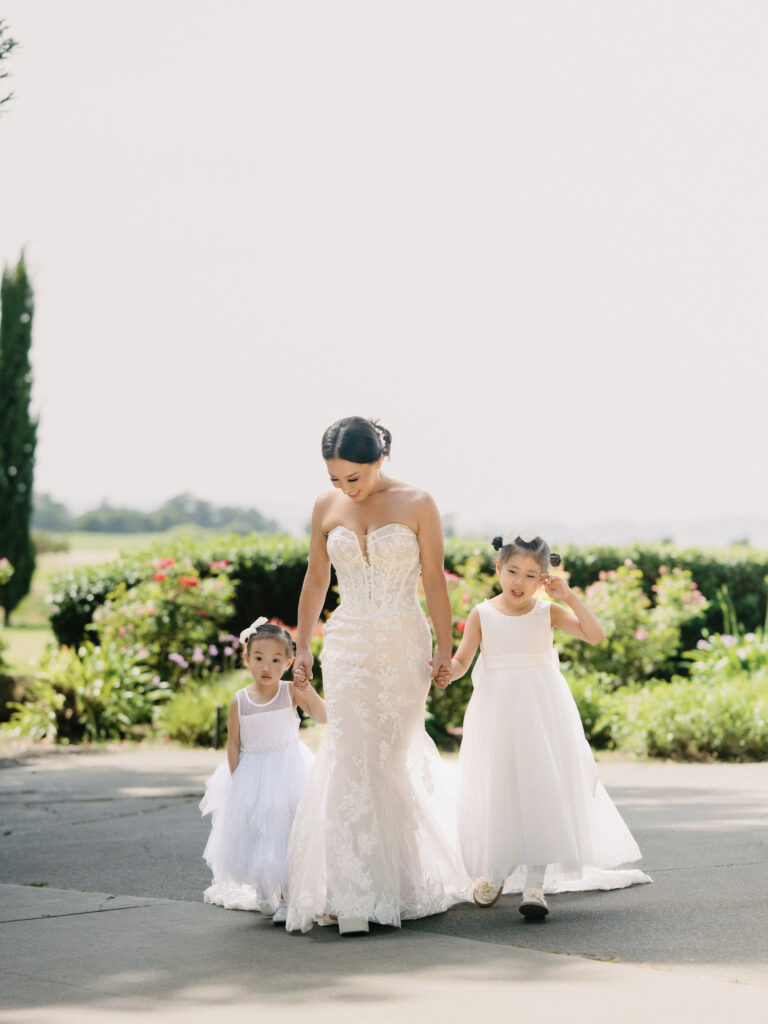 Candid film wedding photography of a beautiful bride walking hand-in-hand with two flower girls, captured by a Napa Valley wedding photographer.