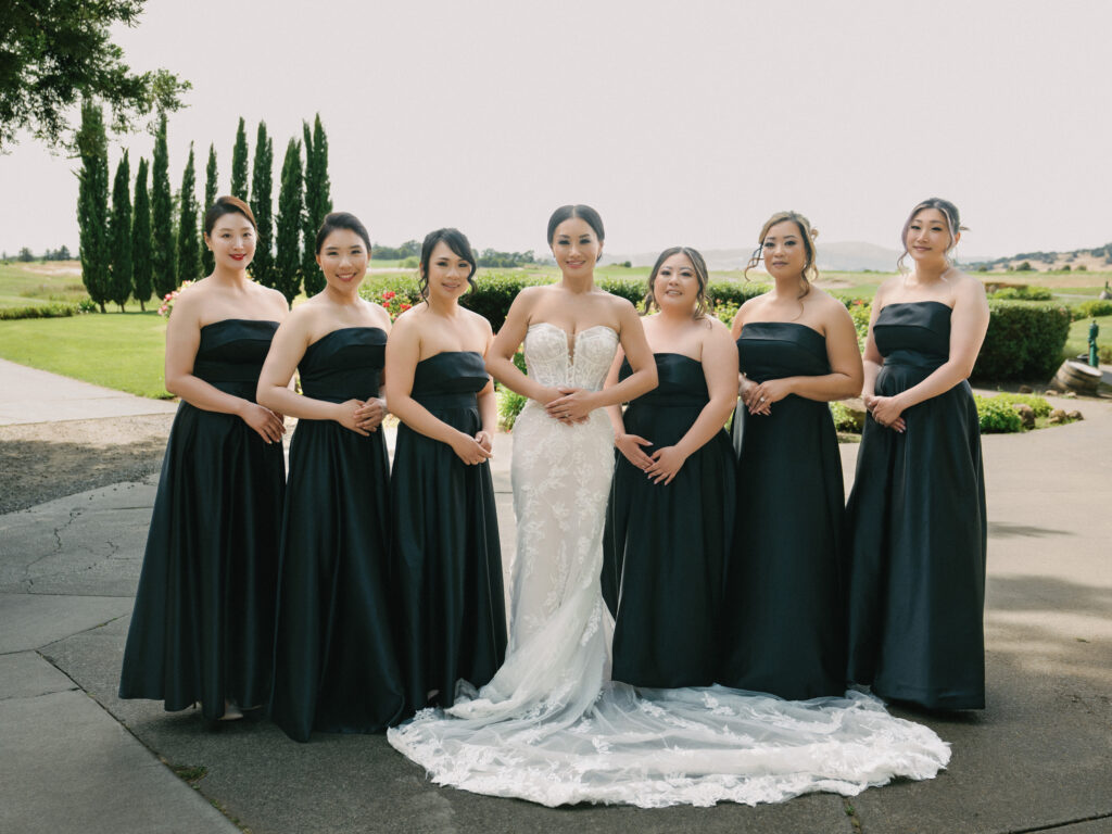 Chic bride in a lace gown posing with bridesmaids in black strapless dresses, shot on film by a Napa Valley wedding photographer.