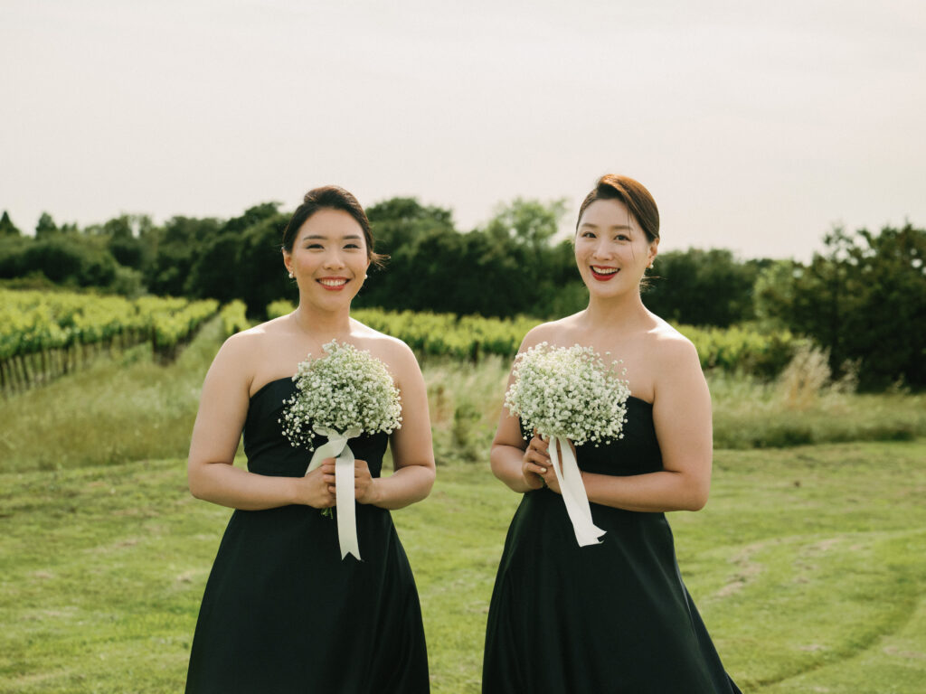 Elegant bridesmaids holding baby's breath bouquets in front of vineyards, captured on film by a Napa Valley wedding photographer.