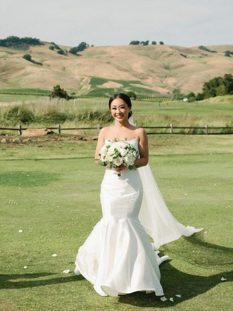 Elegant film wedding photography of a bride holding a white rose bouquet with rolling Napa Valley hills in the background, by a professional photographer.