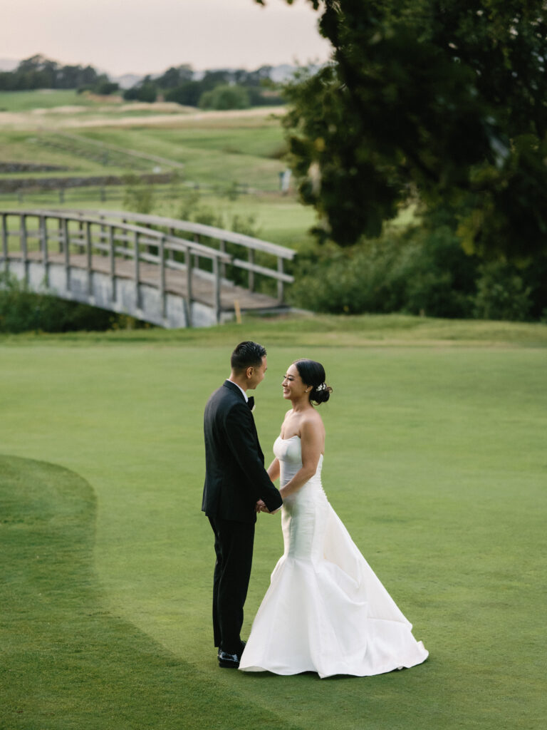 Elegant couple holding hands on an expansive golf course lawn during golden hour, shot on film by a Napa Valley wedding photographer.