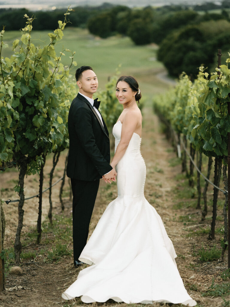 Romantic film wedding portrait of a couple holding hands between lush vineyard rows, captured by a Napa Valley wedding photographer.
