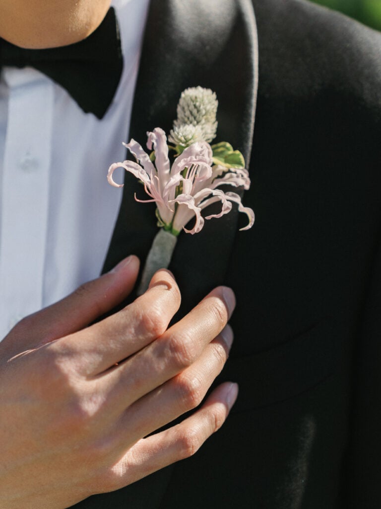 Close-up of a groom's black tuxedo lapel with a unique blush pink and white floral boutonniere, inspiring modern editorial style for destination wedding travel.