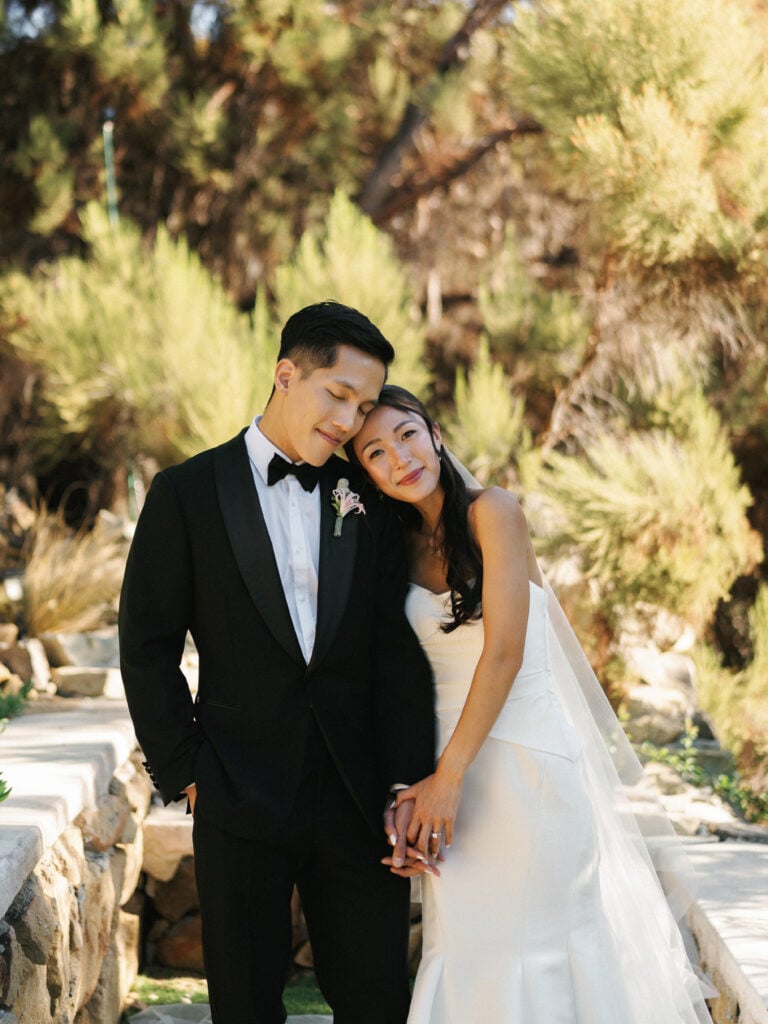 Romantic bride leaning her head on the groom's shoulder while holding hands, showcasing editorial style inspiration for high-end destination wedding travel.