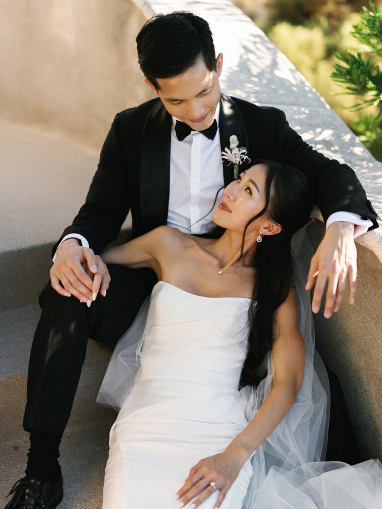 Chic couple sharing an intimate moment sitting on stone stairs, showcasing an elegant strapless satin wedding dress for luxury destination wedding travel inspiration.