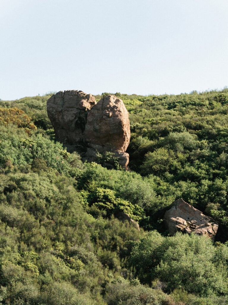 Scenic view of rolling green hills and a massive rock formation in Malibu, a breathtaking backdrop for an exclusive destination wedding travel experience.