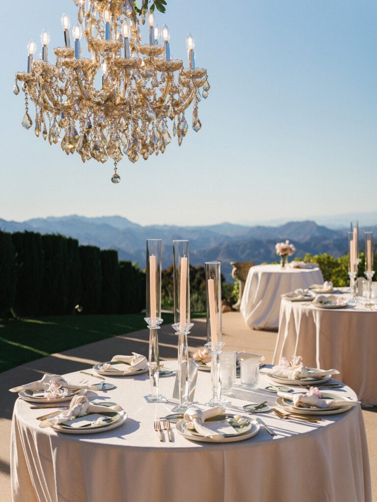 Luxury outdoor wedding reception table setup featuring a crystal chandelier and glass taper candles overlooking mountains, inspiring high-end destination wedding travel design.