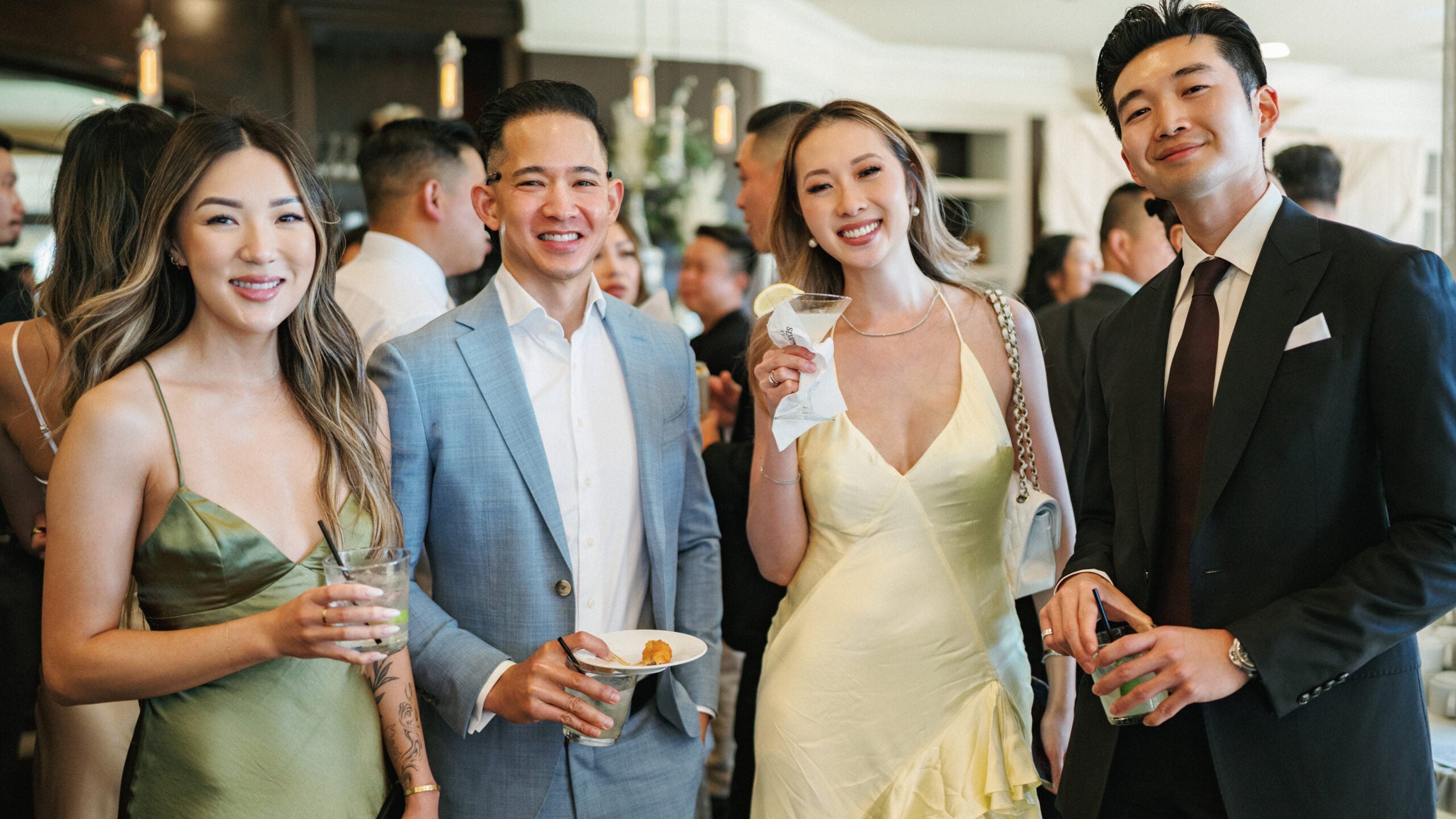 Stylish wedding guests in elegant cocktail attire enjoying drinks and appetizers during an indoor welcome reception as part of professional wedding weekend coverage.