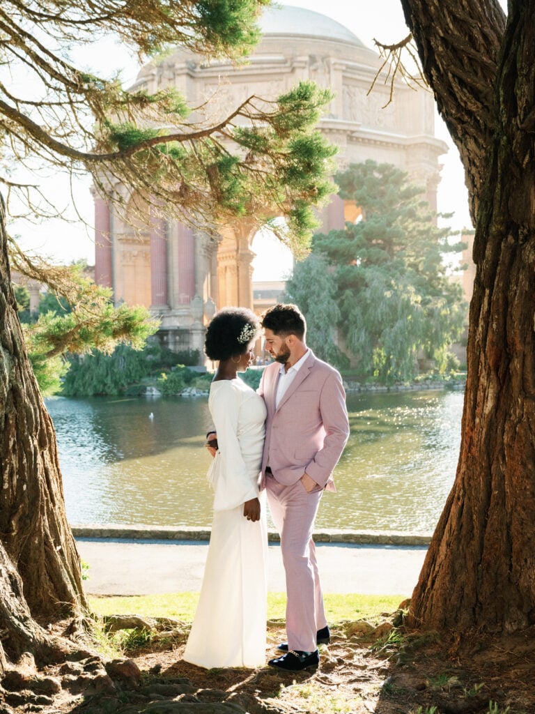 Chic couple embracing by the lake with the Palace of Fine Arts in San Francisco as a backdrop, capturing a natural moment for editorial wedding photography.