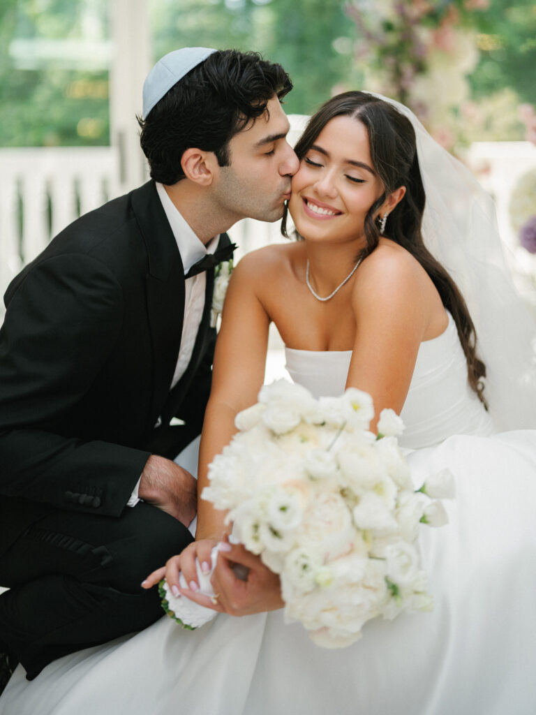 Romantic Jewish wedding photo ideas featuring a groom in a yarmulke kissing his joyful bride on the cheek.