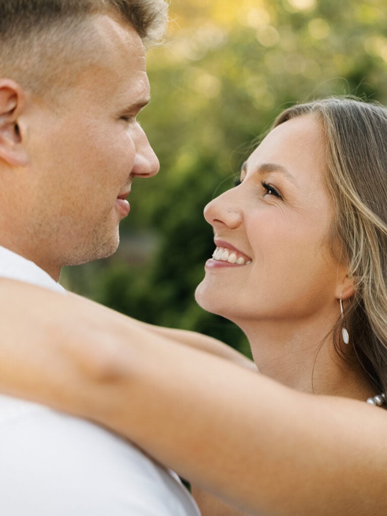 Close-up of a joyful bride with natural glowing makeup smiling lovingly at her groom during a romantic editorial wedding photography session.