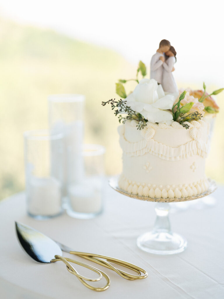 Single tier wedding cake with vintage piping and a couple figurine topper on a glass stand in Big Sur California