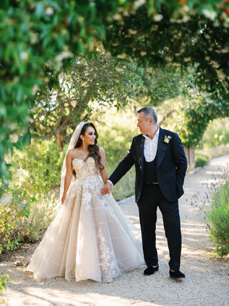 Bride and groom holding hands and talking while walking down a gravel garden path in Big Sur California