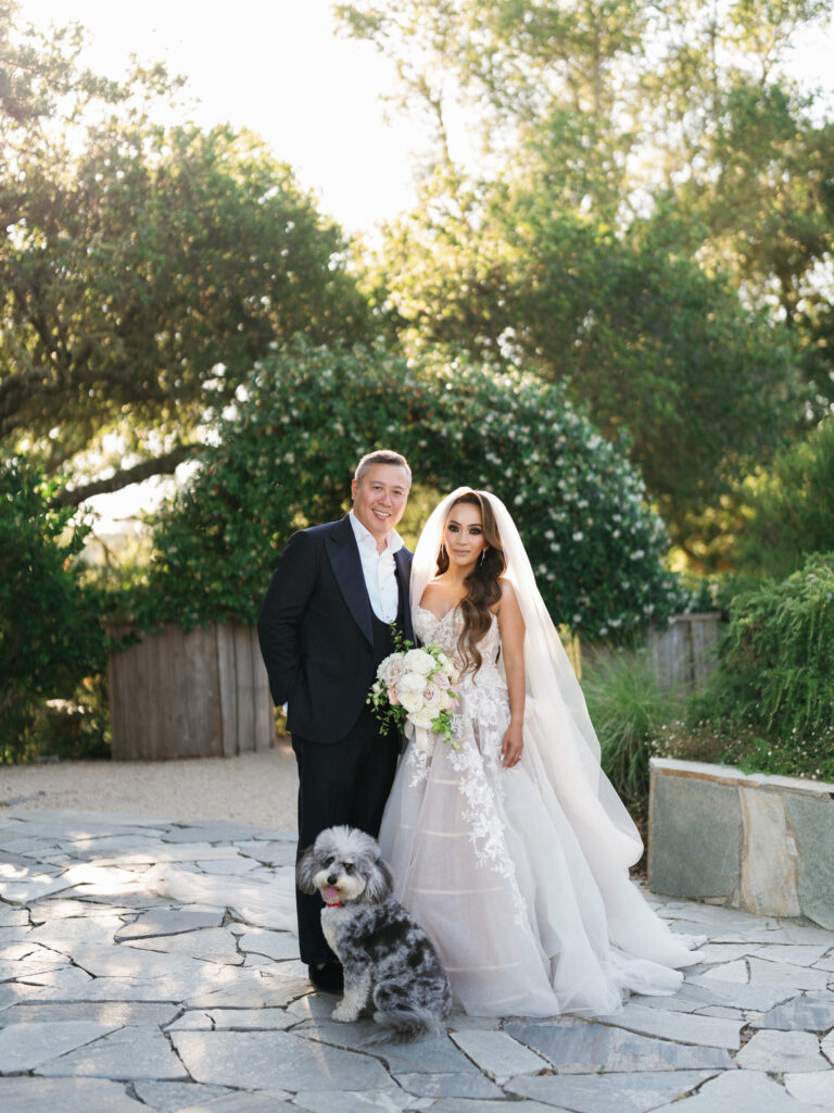 Bride and groom posing with their dog on a stone patio captured by a Big Sur wedding photographer