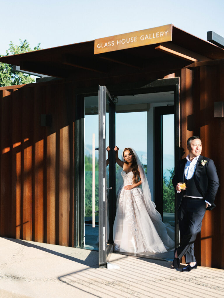 Bride and groom posing in the glass doorway of the Glass House Gallery building with hard afternoon shadows in Big Sur California