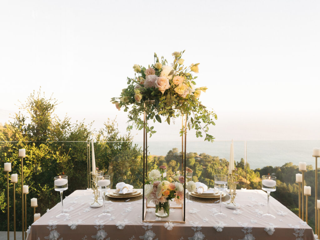Outdoor reception table dinner setup with high floral centerpieces and a panoramic ocean background in Big Sur California