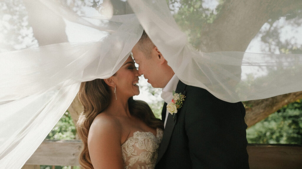 Close up of a bride and groom embracing under a blowing wedding veil with soft backlit sun flare
