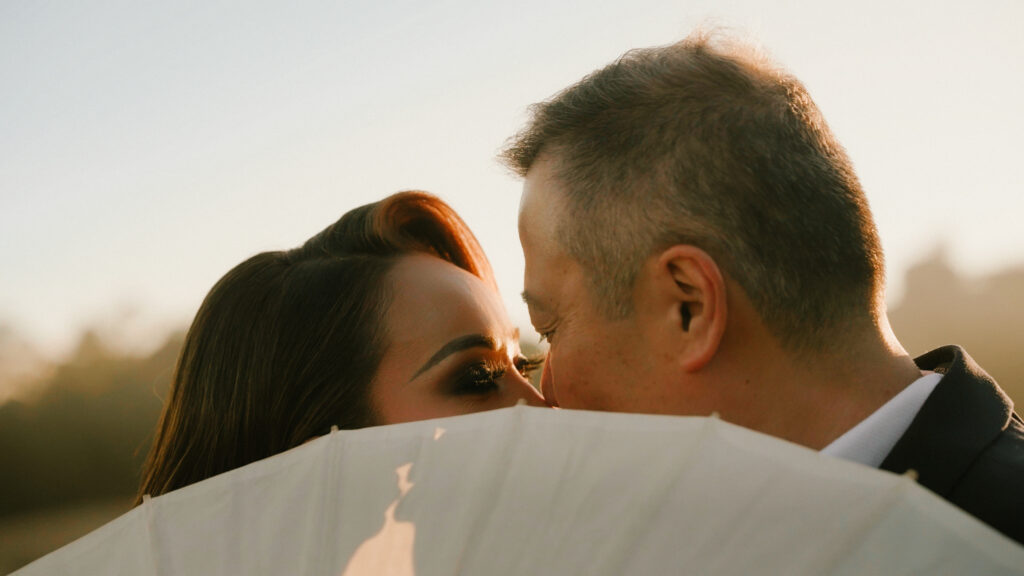 Close up of a bride and groom kissing while hiding behind a white paper parasol during golden hour