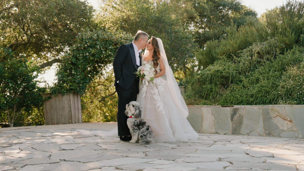 Bride and groom kissing on a stone patio with their fluffy dog standing beside them in Big Sur California