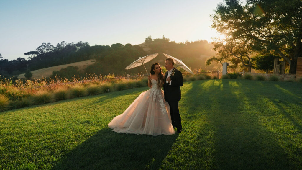 Bride and groom holding white paper parasols on a green lawn during golden hour captured by a Big Sur wedding photographer