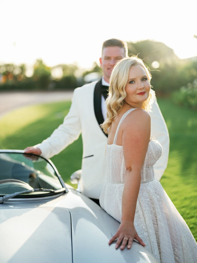 Editorial film wedding photography of a bride in a sparkly corset gown leaning on a vintage silver sports car, captured by a Palm Springs wedding photographer.