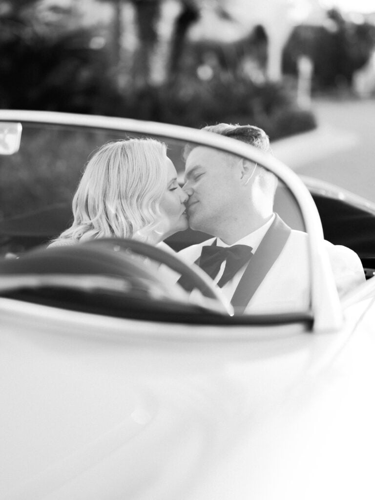 Black and white film wedding portrait of a couple kissing inside a vintage convertible car, taken by a Palm Springs wedding photographer.
