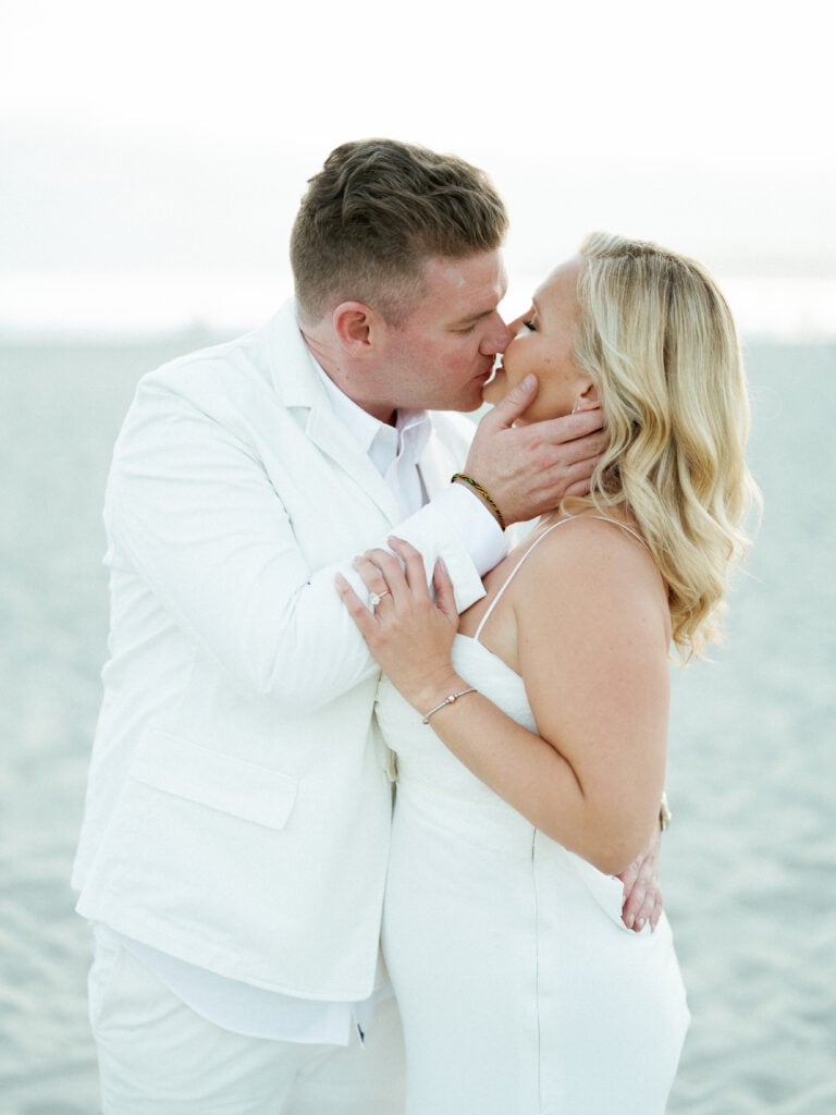 Close-up of a bride and groom in white wedding attire kissing on a beach, captured on film by a Palm Springs wedding photographer.