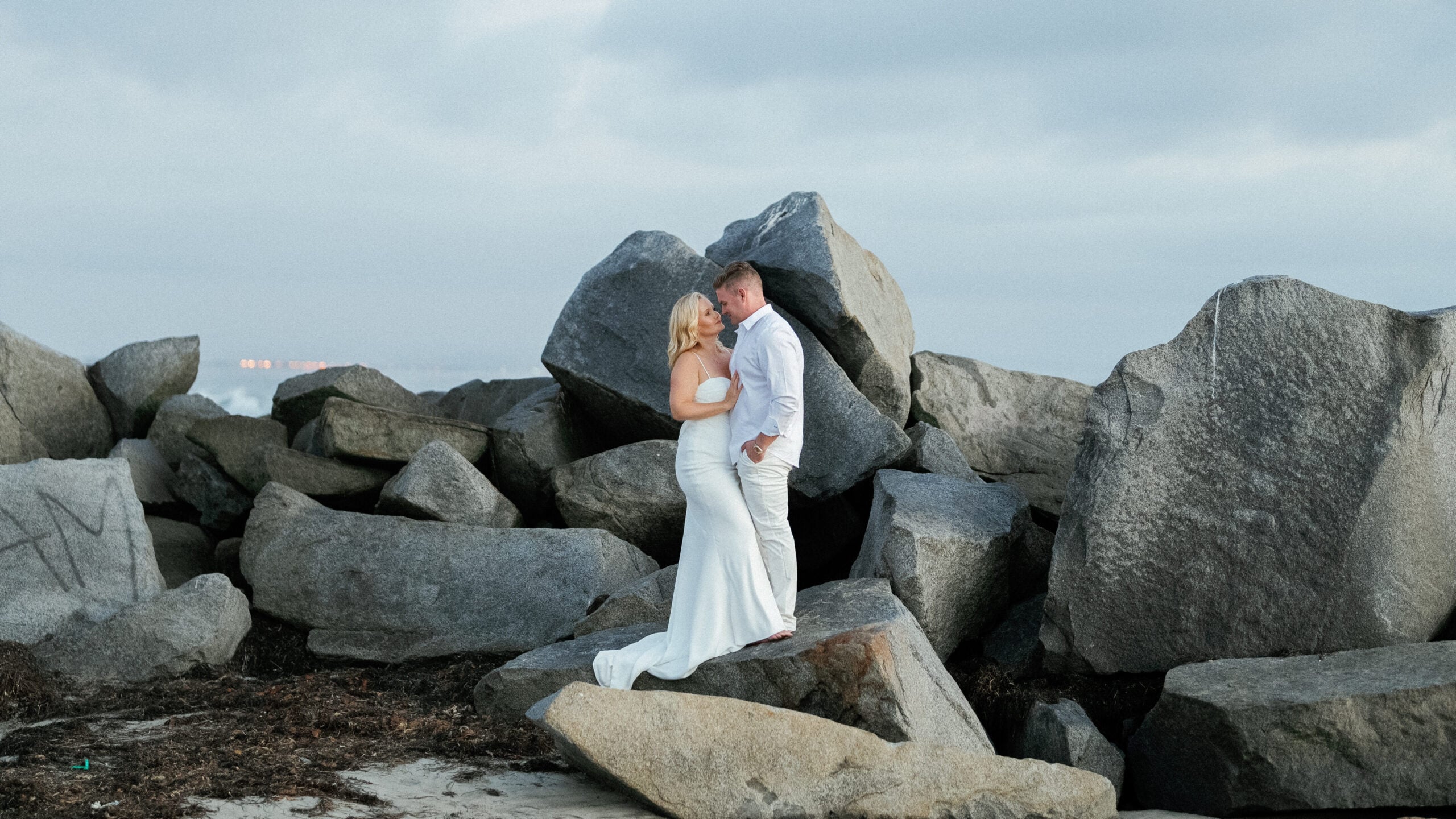 Wide shot of a couple posing on a rocky coastline during a beach elopement, captured on film by a Palm Springs wedding photographer.