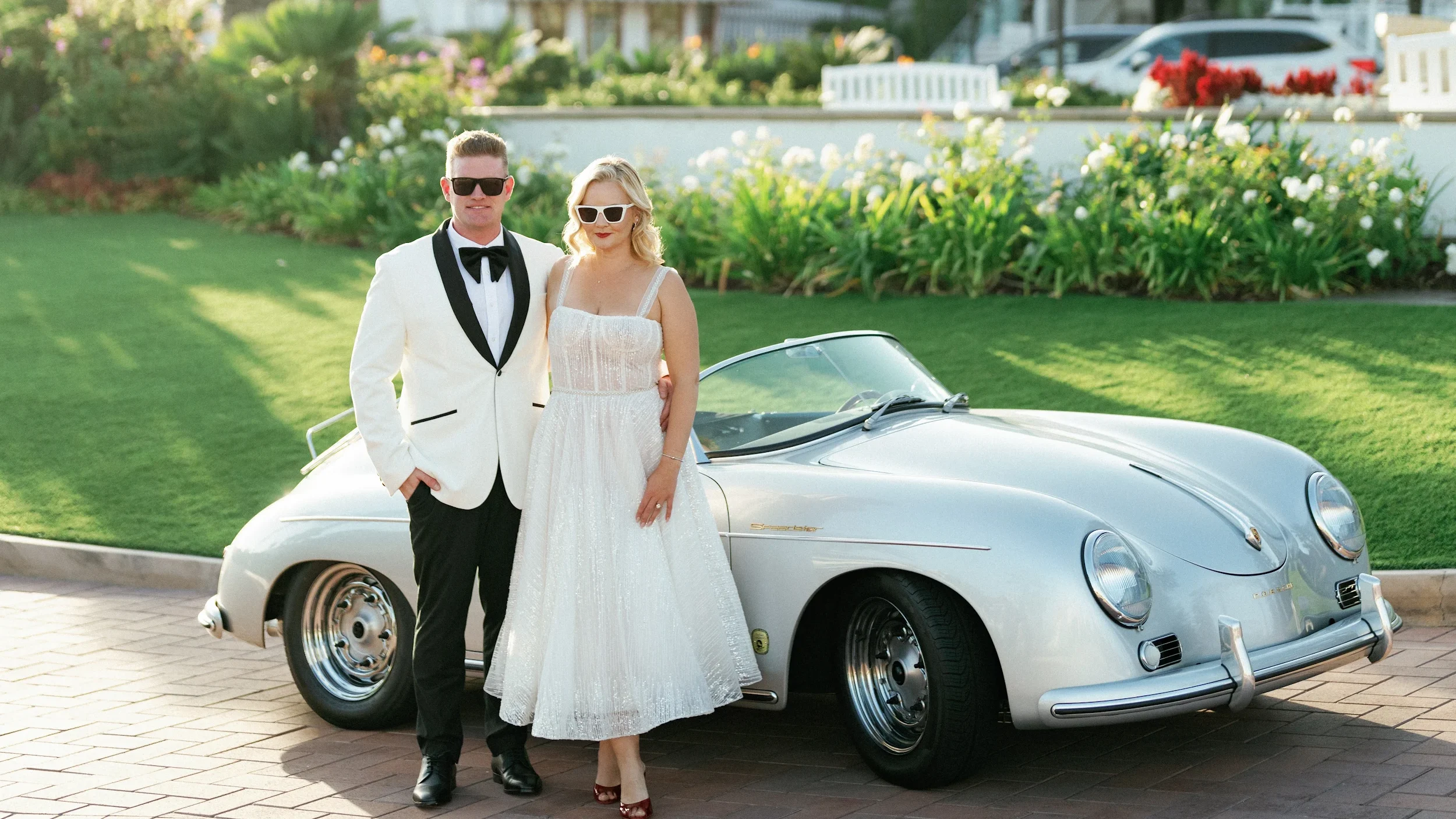 Bride in a tea-length sparkly wedding dress and sunglasses standing by a classic car, shot on film by a Palm Springs wedding photographer.