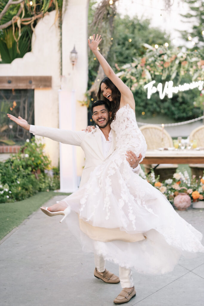 Happy couple celebrating on the dance floor in front of a modern neon sign and luxury floral arch decorations