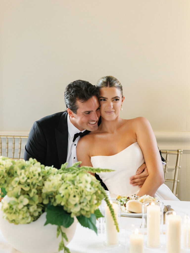 Groom hugging his bride from behind at the dinner table during wedding reception toasts at a luxury estate