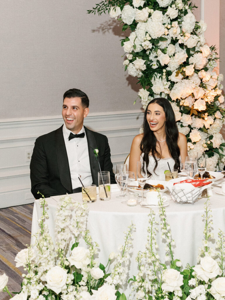 Lush white hydrangea and rose sweetheart table floral backdrop ideas with laughing bride and groom reaction portrait